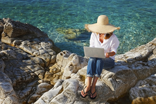Frau sitzt mit Laptop am Meer